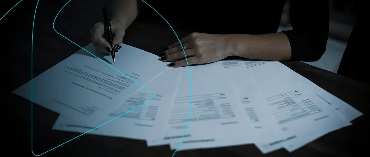 Pessoa assinando contratos e documentos espalhados sobre a mesa