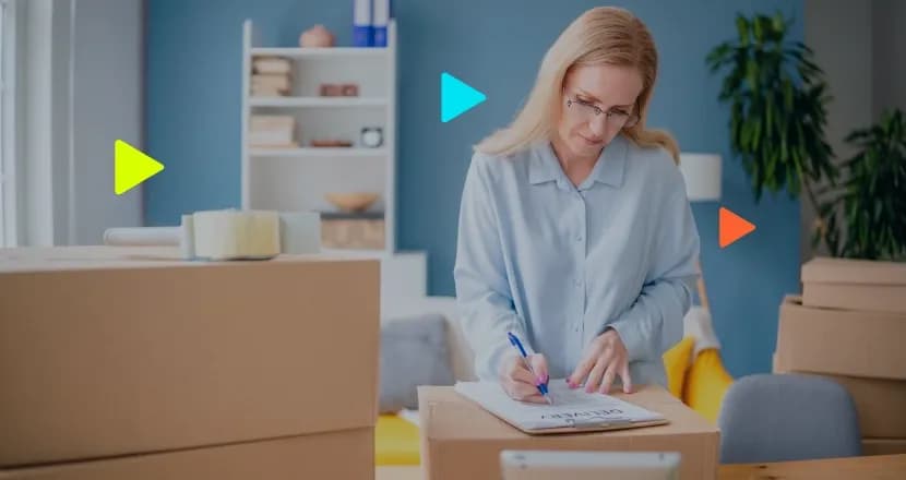 Mulher loira de óculos assinando uma prancheta apoiada em uma caixa de papelão, cercada por outras caixas. Ícones coloridos de 'play' sobrepostos à imagem.