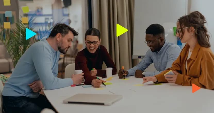 Quatro profissionais sentados ao redor de uma mesa branca em um escritório moderno, sorrindo e colaborando em uma reunião. Eles estão escrevendo e organizando post-its coloridos sobre a mesa. O grupo é diverso, composto por dois homens e duas mulheres. Há um notebook fechado em primeiro plano e, ao fundo, um vidro com post-its e um quadro branco. Ícones geométricos coloridos em formato de 'play' aparecem sobrepostos à imagem.