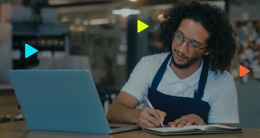 Homem escrevendo em um caderno enquanto usa laptop.