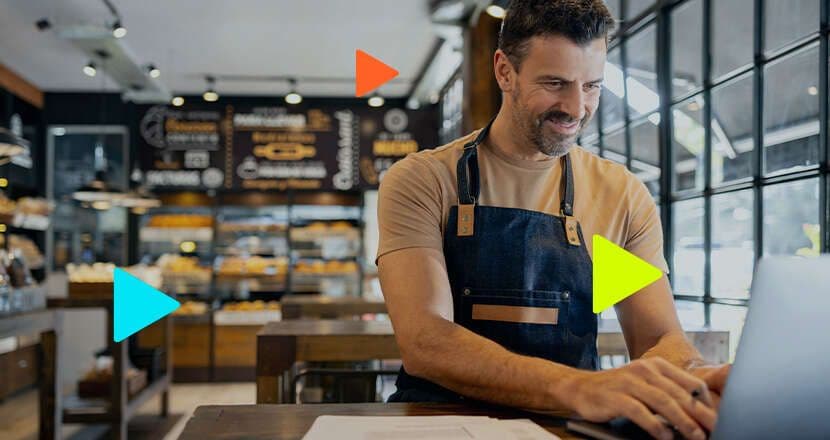 Homem sorridente trabalhando em cafeteria com laptop