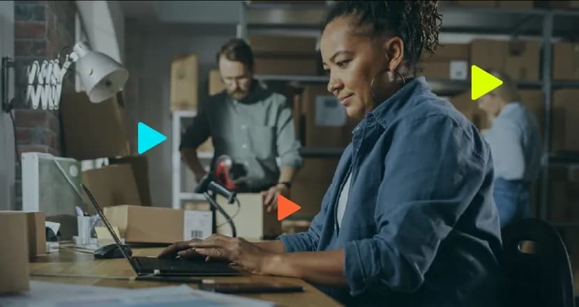Mulher trabalhando em mesa com laptop e caixas ao fundo.