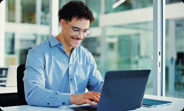 Profissional sorrindo enquanto trabalha em um notebook no escritório