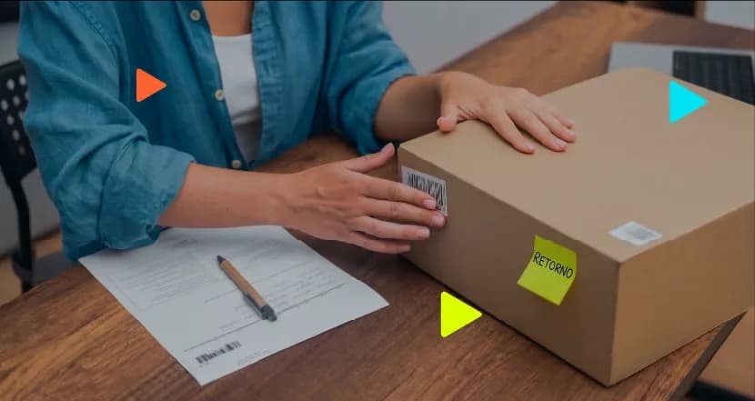 Mãos sobre caixa de papelão com adesivo de retorno ao lado de documento em mesa de escritório.