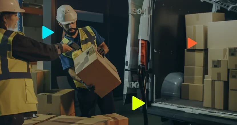 Trabalhadores de capacete e colete a ler código de barras de caixa junto a carrinha de carga.