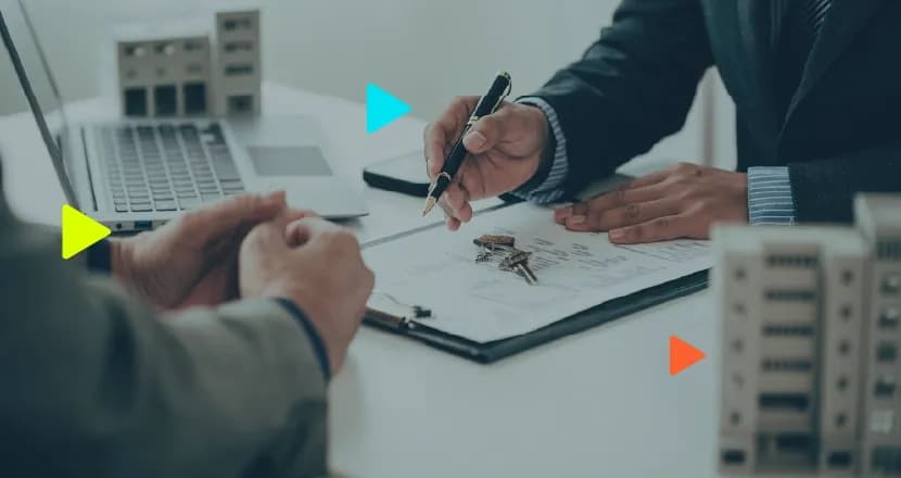 Corretor e cliente em reunião assinando contrato imobiliário com chaves e maquetes de prédios sobre a mesa.