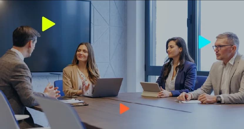 Grupo de profissionais em reunião de consultoria empresarial ao redor de uma mesa com notebook e tablet.
