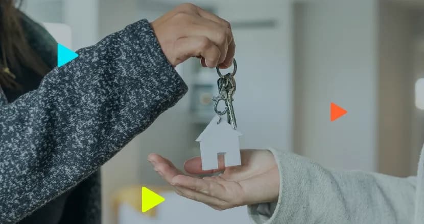 Close de corretor de imóveis entregando chaves com chaveiro em formato de casa para a mão de um cliente.