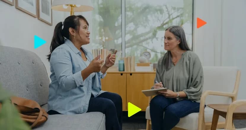 Paciente conversando no sofá com psicóloga que faz anotações em consultório.