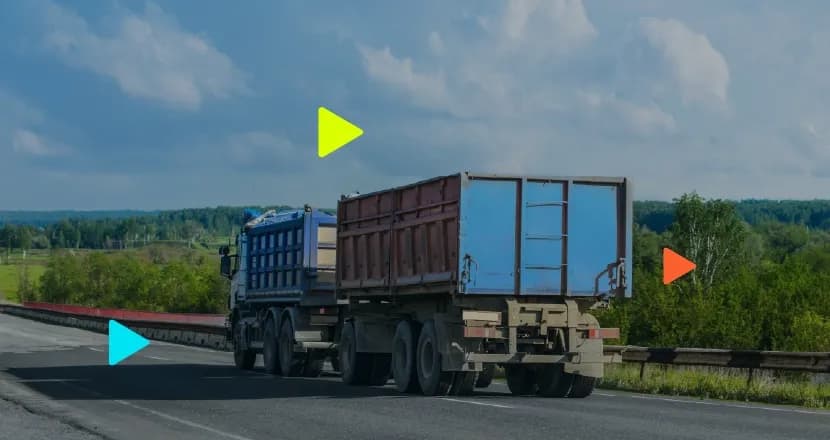 Caminhão de carga com reboque duplo trafegando em rodovia asfaltada com vegetação ao fundo.