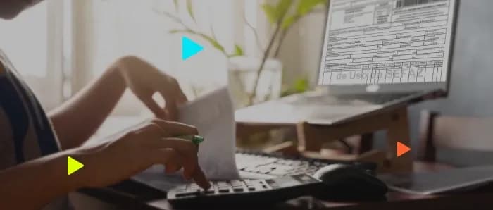 Pessoa usa calculadora e analisa documentos fiscais. Ao lado, notebook exibe o DANFE de uma Nota Fiscal Eletrônica.