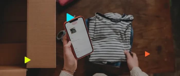 Vista superior de mãos segurando celular para anunciar blusa listrada ao lado de caixa de papelão.