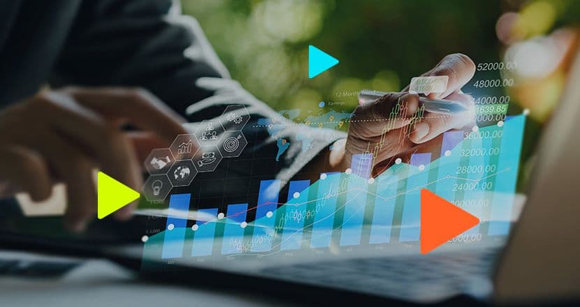 Mãos de um profissional a apontar com uma caneta para o ecrã de um computador portátil, com uma sobreposição de gráficos financeiros digitais, barras de estatísticas luminosas e ícones de negócios.
