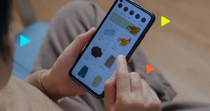 Pessoa segura smartphone e usa o dedo para navegar em um aplicativo de compras com catálogo de roupas e calçados.