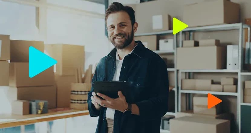 Empreendedor sorridente segurando tablet em estoque com caixas de papelão.
