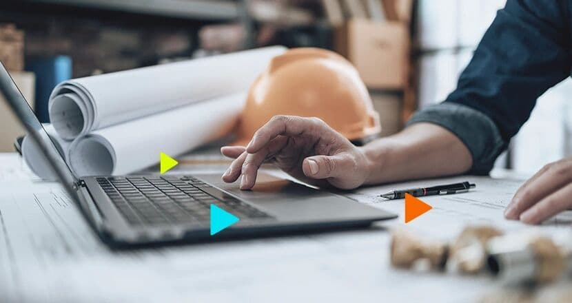 Mão usando laptop sobre mesa com projetos de construção