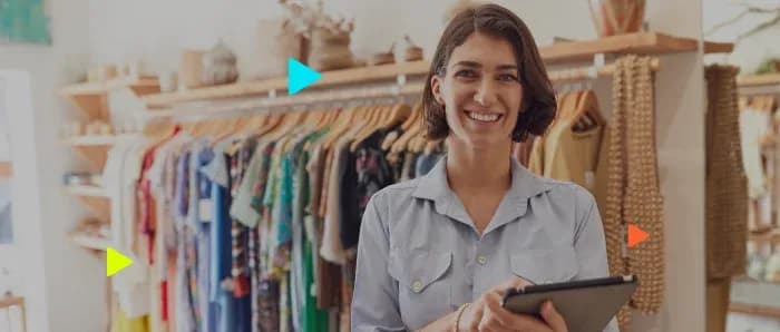 Mulher sorrindo em loja de roupas com tablet na mão.