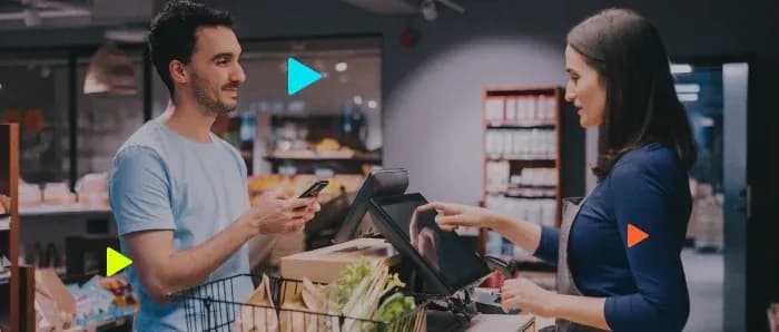 Atendente opera tela do caixa enquanto cliente segura celular para pagar compras em um mercado comercial.