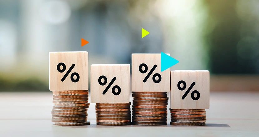 Pilhas de moedas com blocos de madeira e símbolos de porcentagem, representando o empréstimo MEI