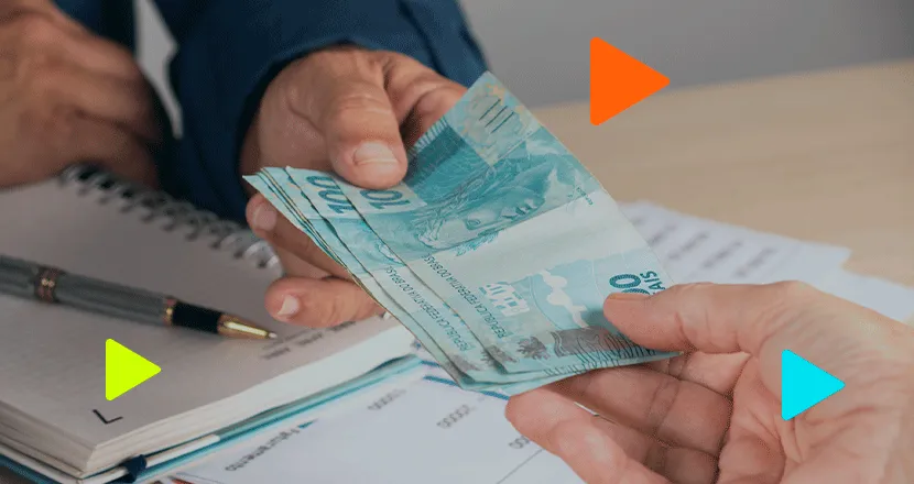 Transação em dinheiro com notas de 100 reais em ambiente de escritório, com elementos gráficos coloridos flutuantes.