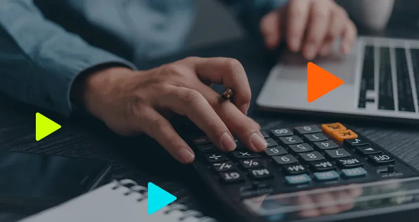 Pessoa realizando cálculos manuais em calculadora preta ao lado de laptop.