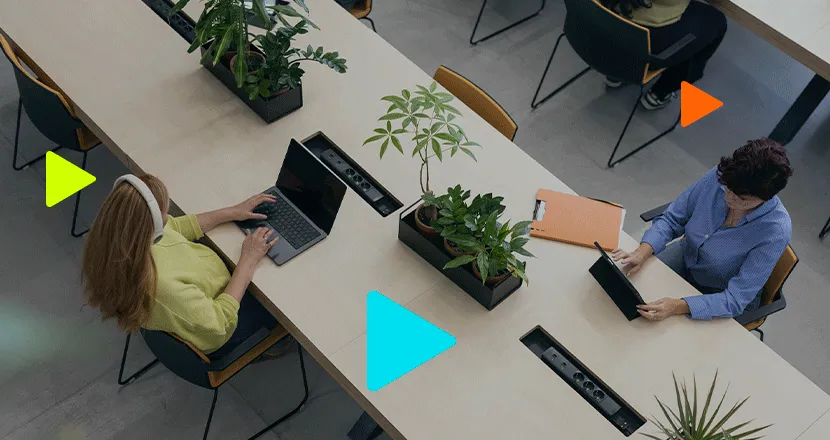 Vista aérea de duas mulheres trabalhando em mesa de escritório compartilhada com laptops.