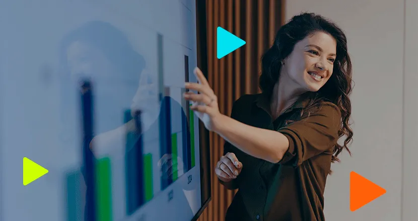 Mulher sorridente apontando para gráfico de barras em tela digital durante apresentação de resultados empresariais.