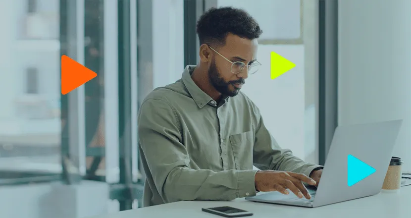 Jovem desenvolvedor negro concentrado trabalhando no notebook em escritório moderno com ícones de play coloridos.