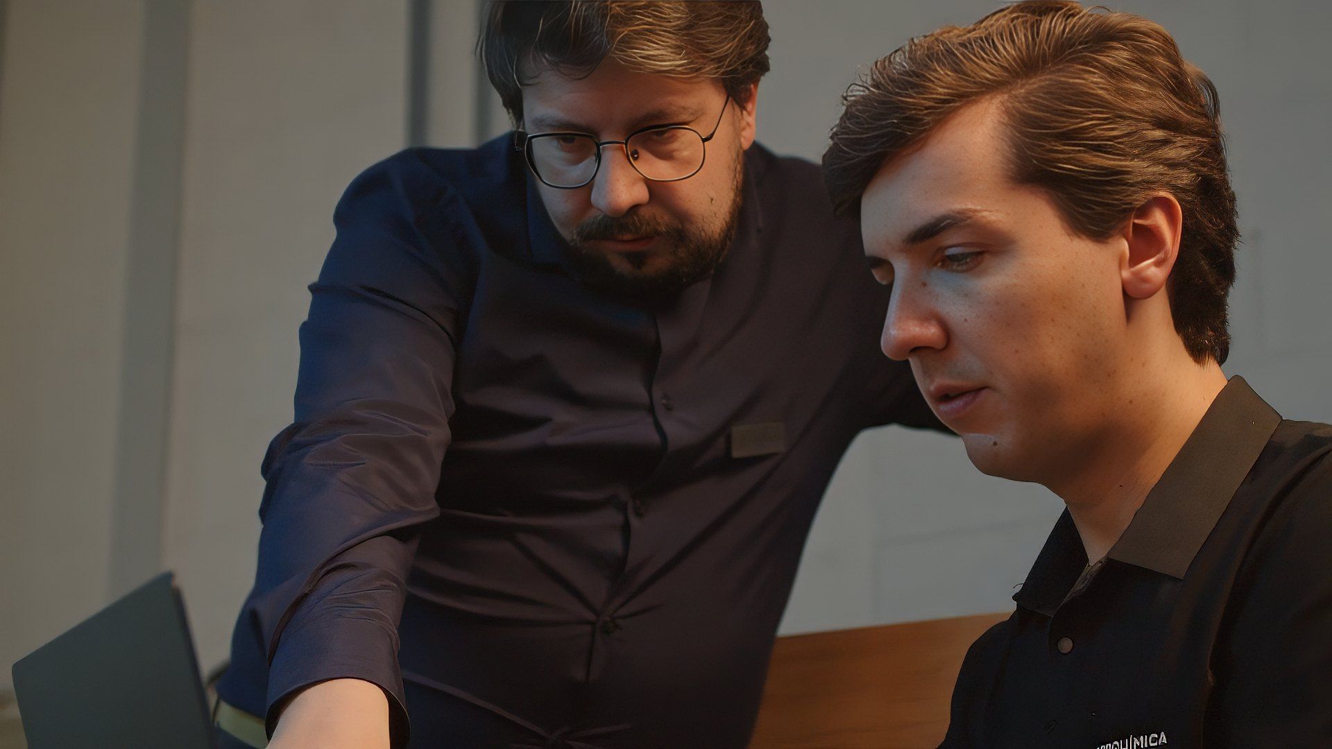 Dois profissionais da Hipperquimica olham juntos para a tela de um notebook: o gestor, de camisa e oculos, aponta para o monitor enquanto o colega de polo preta acompanha a informacao na tela.
