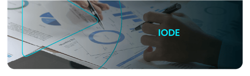 Capa da seção IODE: mãos analisando relatórios com gráficos financeiros, com o texto IODE em destaque.